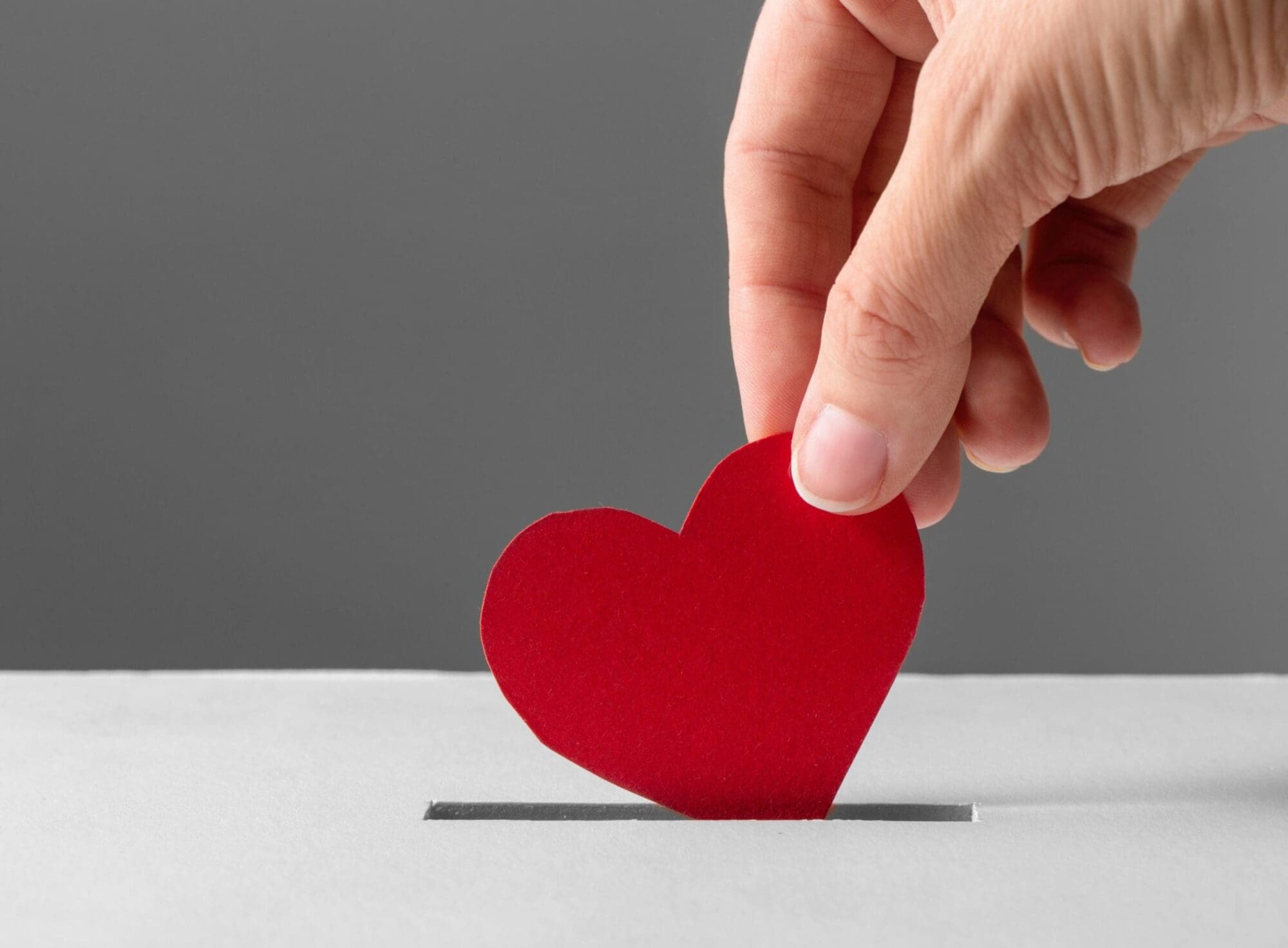 Hand putting red paper heart into box_2500x1800 Hand putting red paper heart into box