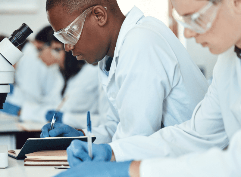 A photo of a man and woman wearing googles in a lab writing things down in a notebook.