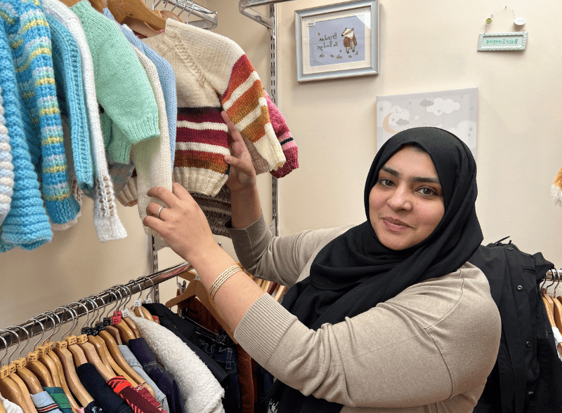 A photo of a woman smiling as she looks through a rail of clothes.