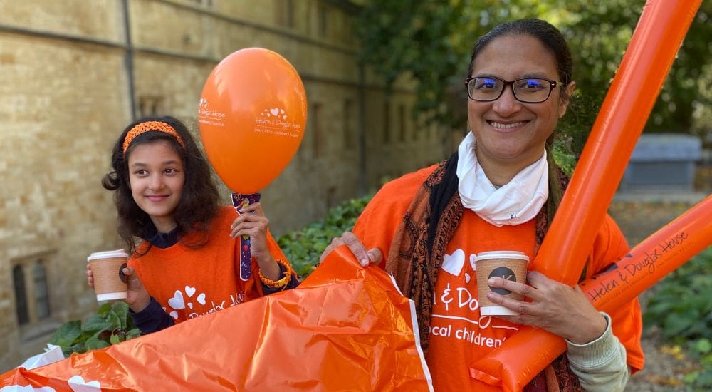 Anvita Anvita, an events volunteer, and a young girl holding a Helen & Douglas House banner and balloons.