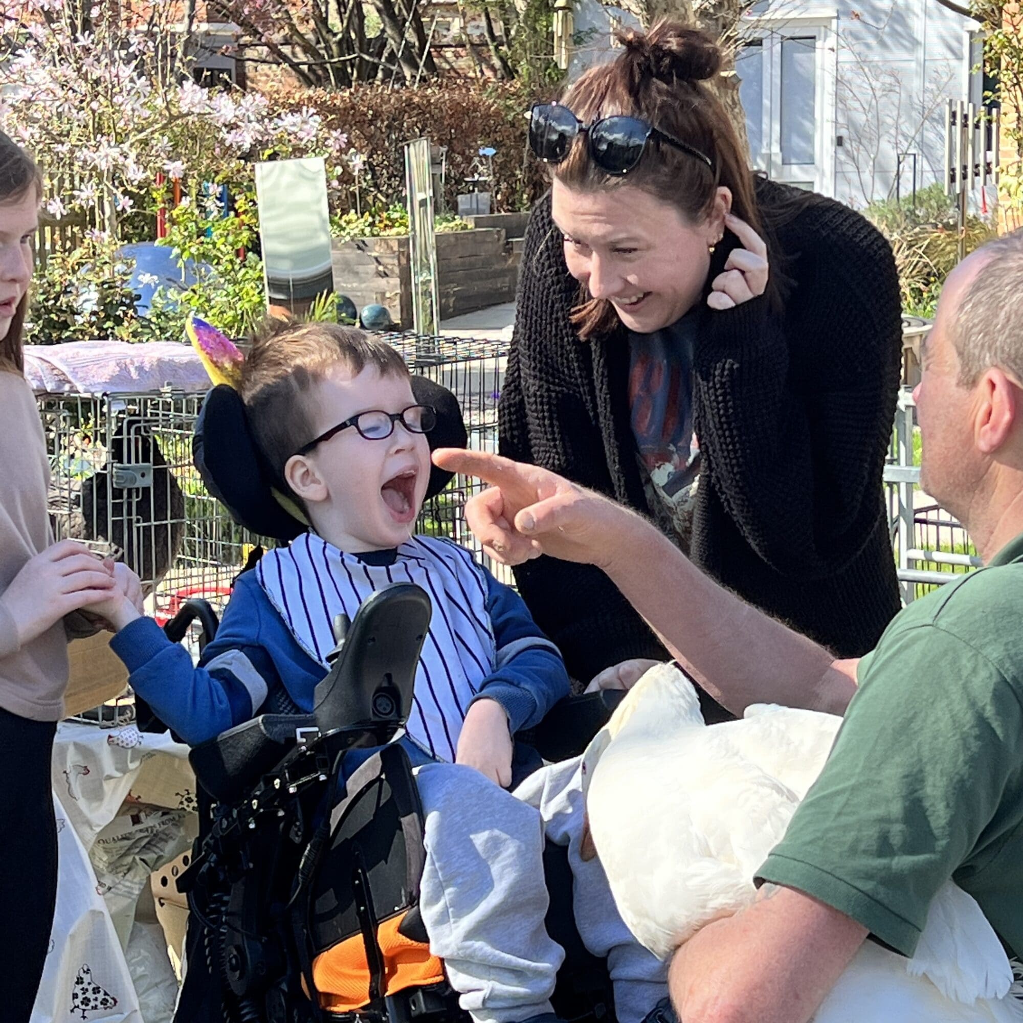 a boy in a wheelchair smiling with his mum next to him and man in a green top holds a goose