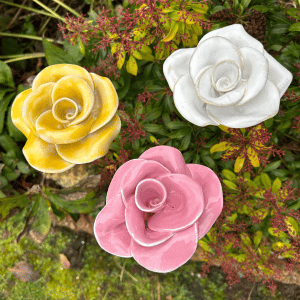 A pink, white and yellow glazed ceramic rose standing in a flowerbed.