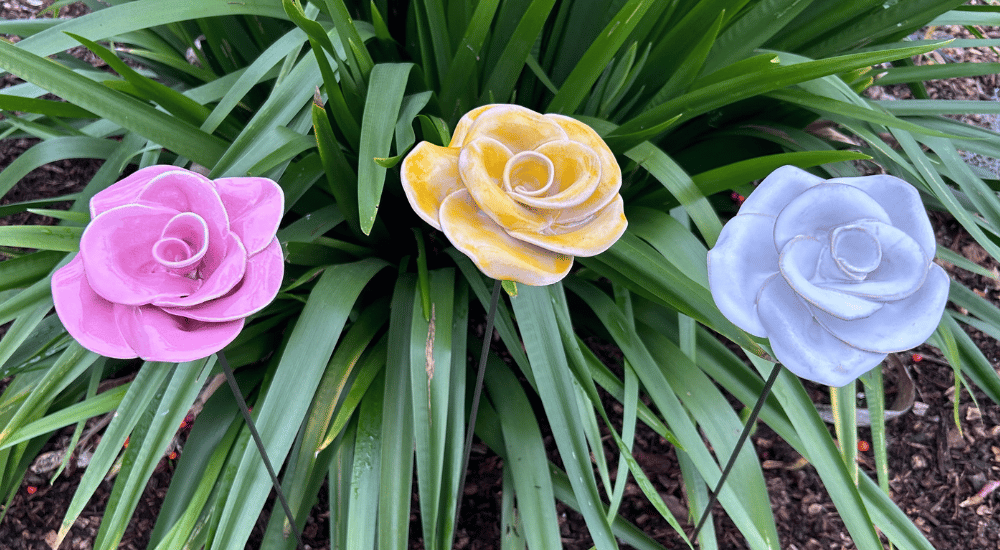 Three roses landscape light yellow A pink, white and yellow glazed ceramic rose standing in front of a green plant.