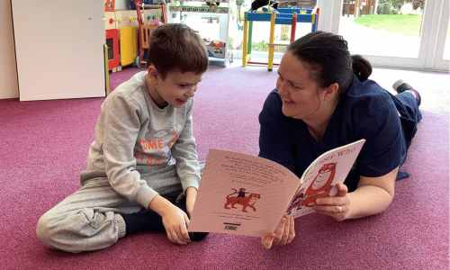 A female nurse and a young boy sitting on the floor reading together