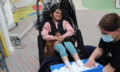 A young girl in a wheelchair. A female nurse is covering the girl's feet in foam.