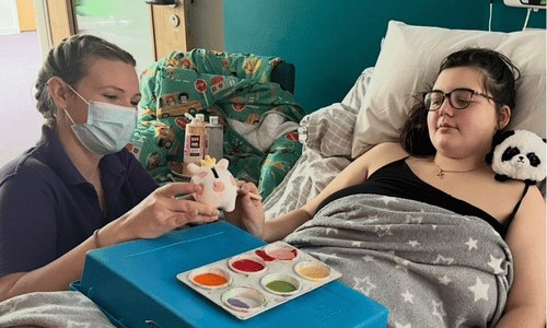 A young girl in a wheelchair. A female nurse is covering the girl's feet in foam. 