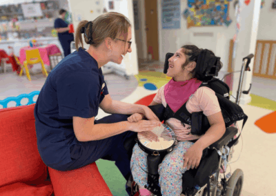 A female nurse and a girl in a wheelchair playing the tambourine together
