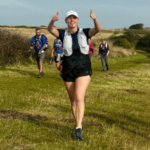 A young woman with her thumbs up running across grass