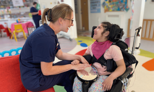 A nurse and a girl in a wheelchair are smiling at each other whilst playing the tambourine