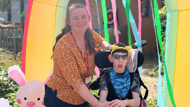 A young boy in a wheelchair with his mum under a yellow inflatable arch