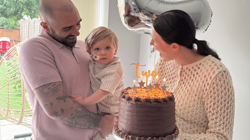 Calum, and faith smiling at Bobby and showing him a big birthday cake