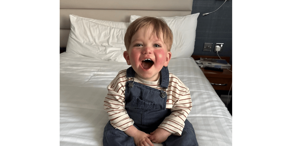 A young boy, Bobby, sitting on a bed and smiling.