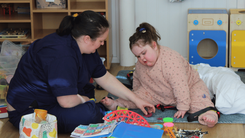 Nurse playing with Ella A female nurse and a young girl are sitting on the floor playing with toys